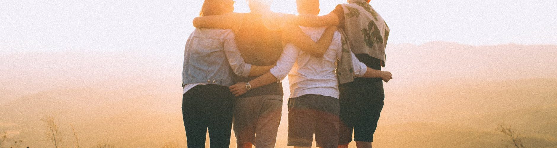 four person standing on cliff in front of sun