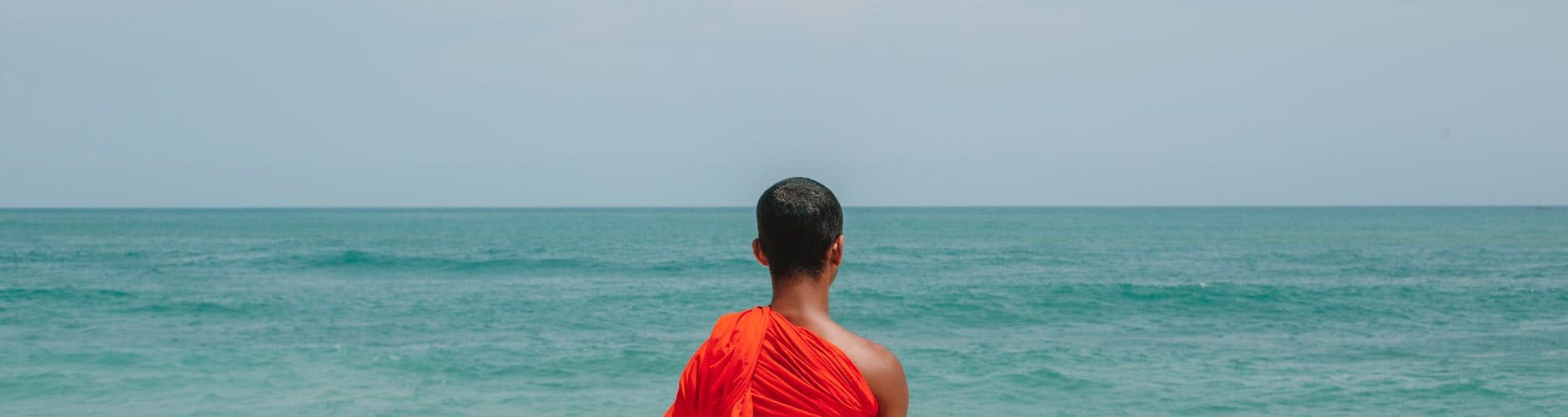 unrecognizable asian male monk in traditional orange robe on seashore