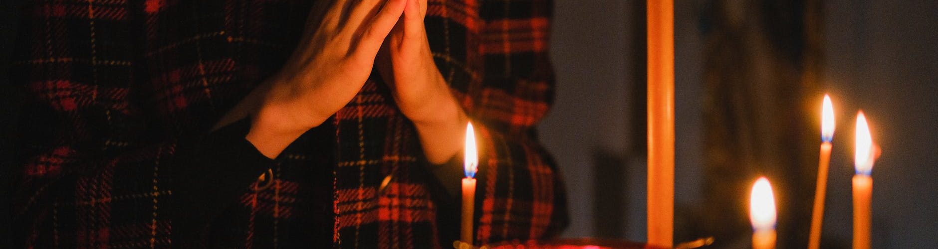 person in red and black plaid long sleeve shirt praying before lighted candles