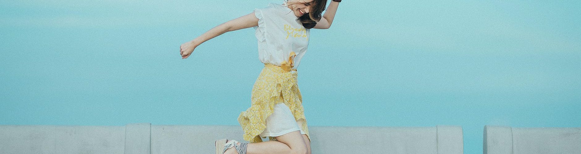 jumpshot photography of woman in white and yellow dress near body of water