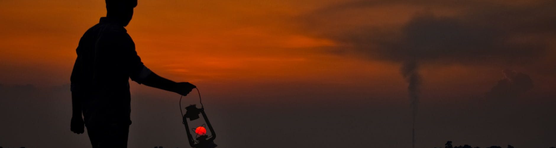silhouette of man with oil lamp on shore at sunset