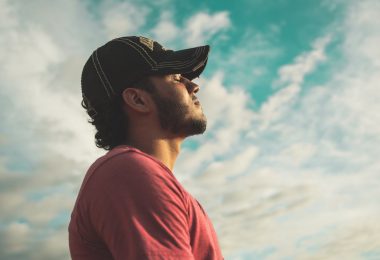 man wearing black cap with eyes closed under cloudy sky