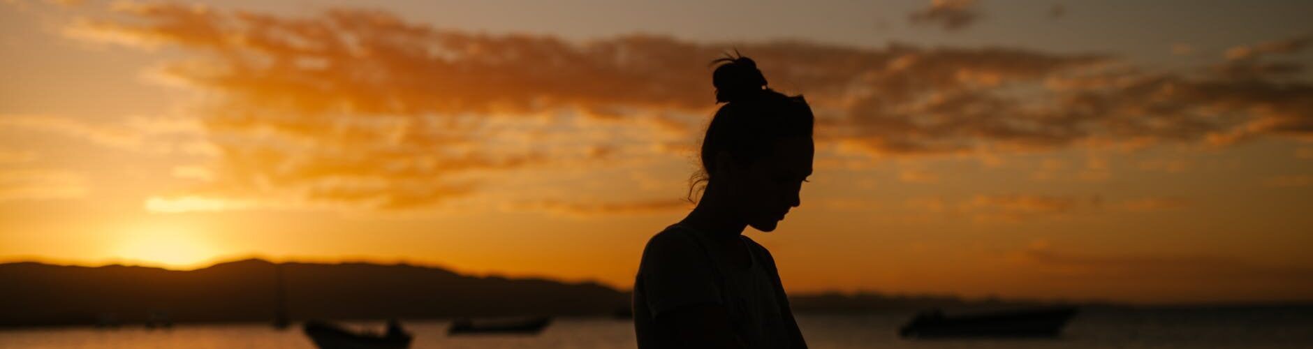 sad woman standing on coast of sea at sunset