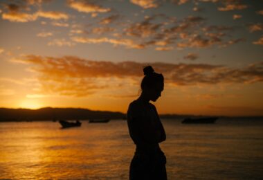 sad woman standing on coast of sea at sunset