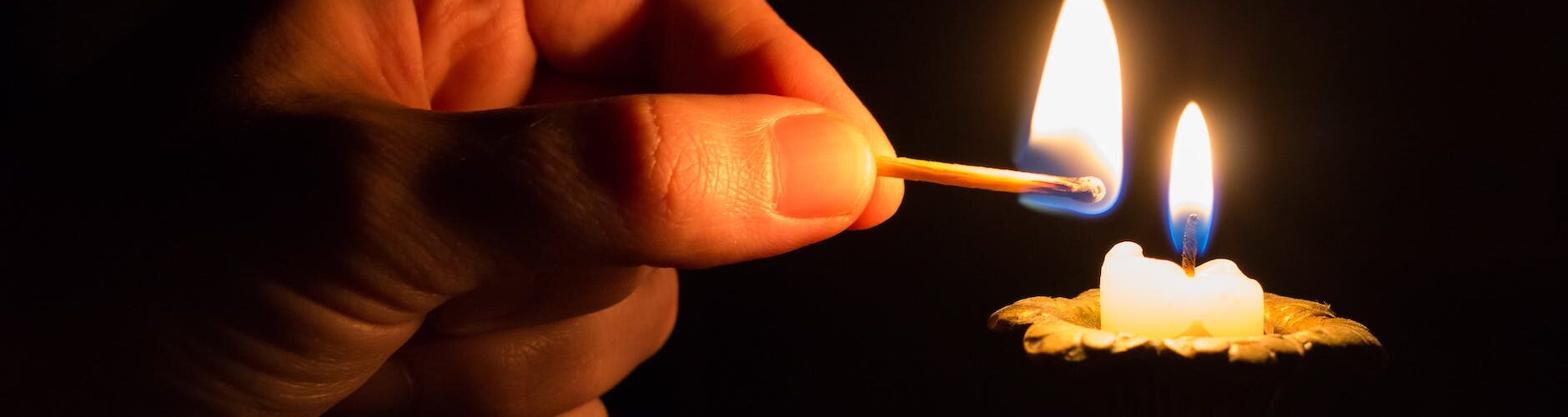 person holding match stick with fire in front of candle with fire