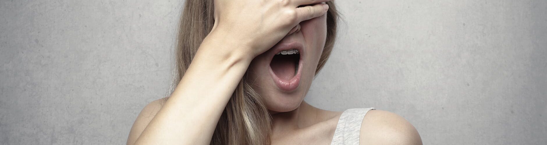 woman in gray tank top covering her face with her hand