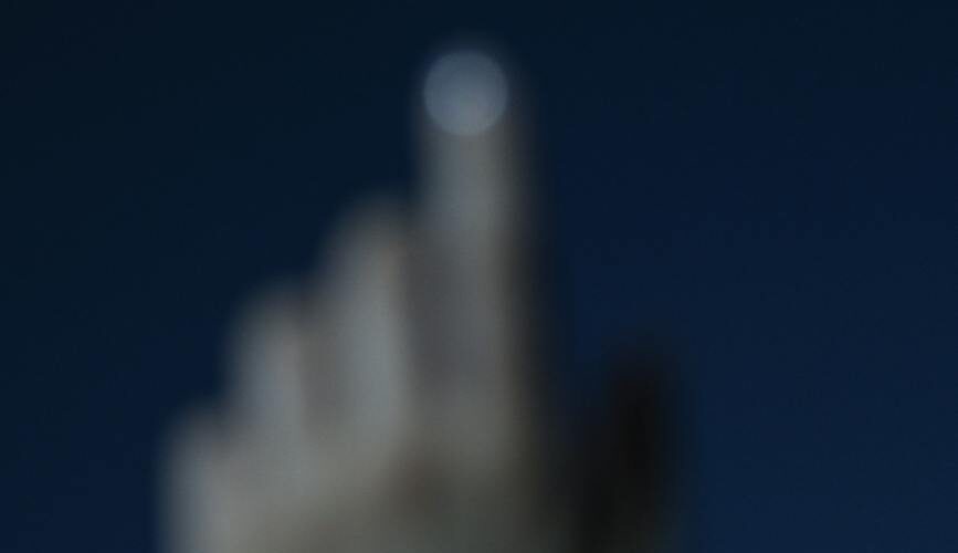 photo of a blurred hand and finger point to the moon at night