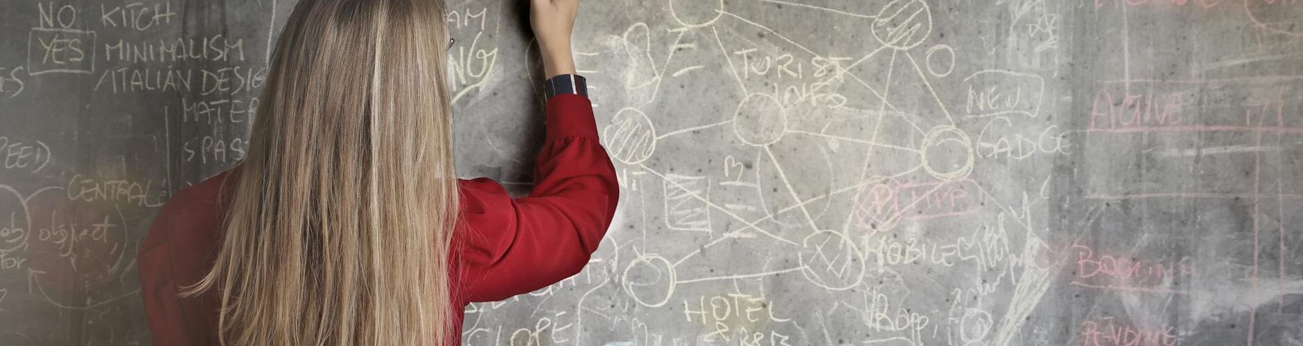 woman in red long sleeve writing on chalk board