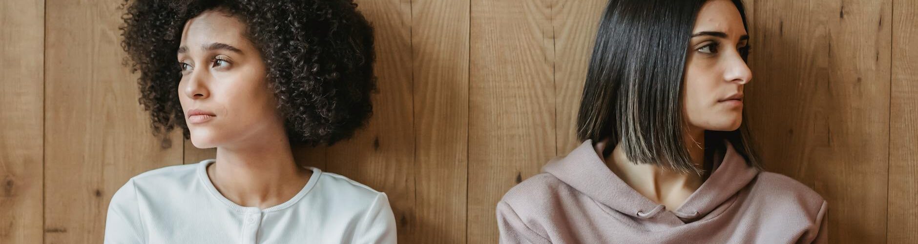 pensive multiracial women near wooden wall looking away