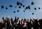 newly graduated people wearing black academy gowns throwing hats up in the air