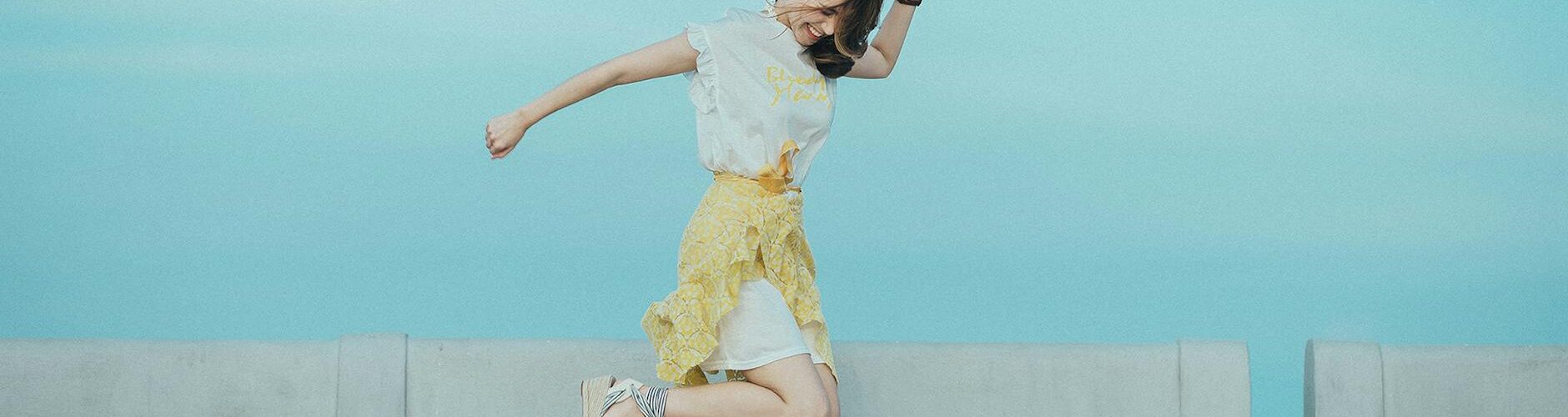 jumpshot photography of woman in white and yellow dress near body of water