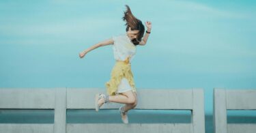 jumpshot photography of woman in white and yellow dress near body of water